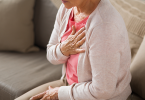 Older woman sitting on sofa with hand over heart.