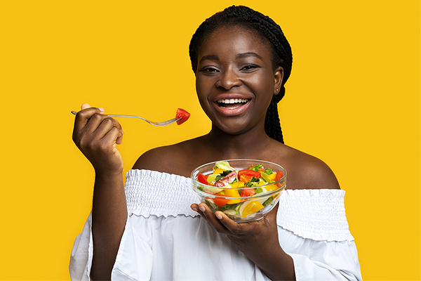 Black woman smiling and eating bowl of fruit