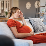 Pregnant woman in pain sitting on sofa